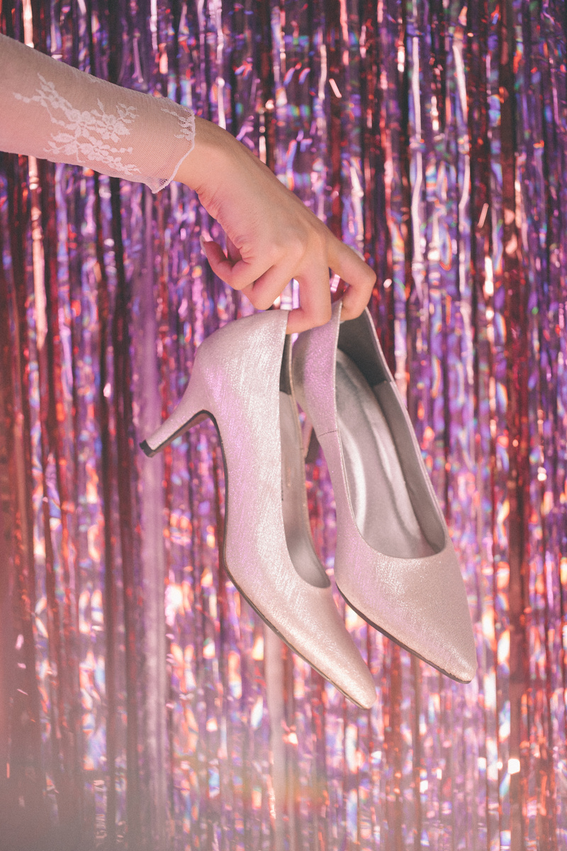 Female Hand Holding a Pair of Shoes against Shiny Background